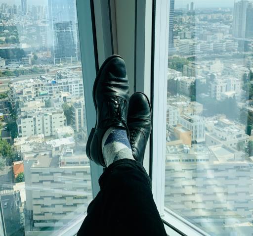 A city skyline from an office window. A man in office wear has his feet crossed out to the view.