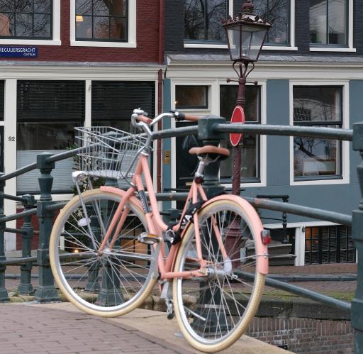 A pink bike with a basket attached to a canal bridge in Amsterdam.