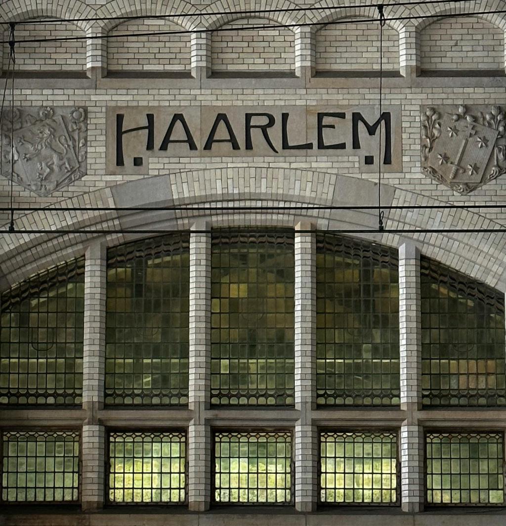 Haarlem Station – a gray brick building with 'Haarlem' inscribed, flanked by two crests. Below, green glass offers a look into the station.