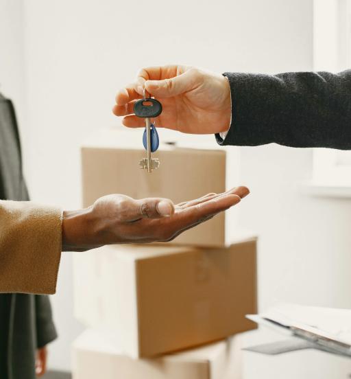 A person in a suit handing keys to another person. Moving boxes are in the background.