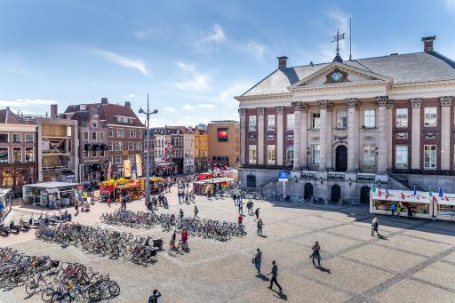 Groningen City Hall, surrounded by a square. People walk about, some on bikes that are lined up in rows.