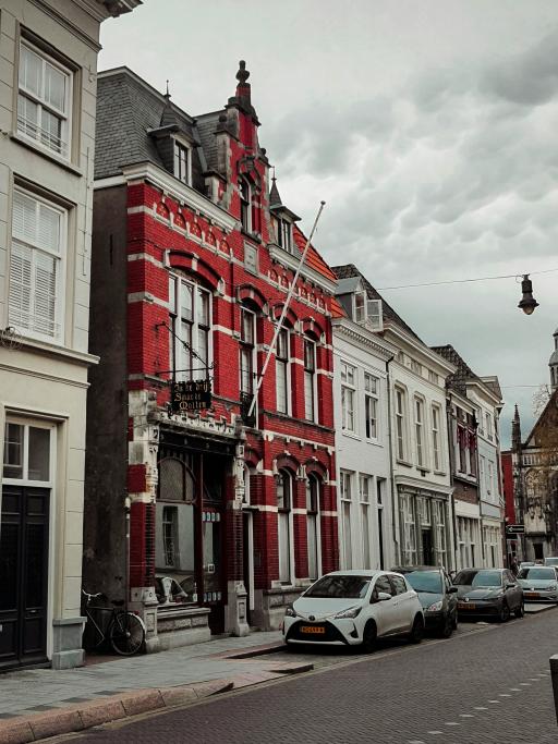 A row of buildings on a Dutch street. Cars are parked up outside. The main focus is a red building.