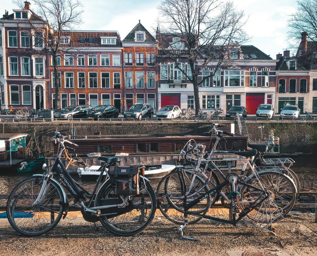 Een uitzicht op Groningen. Een kanaal met fietsen langs het water. Aan de overkant staan huizen met geparkeerde auto's.