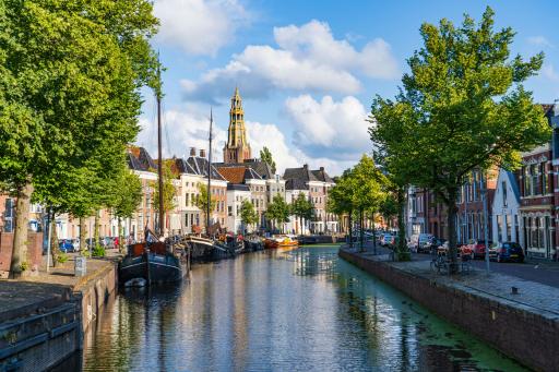 Boats on a canal in Groningen, the Netherlands. The sky is clear and green trees line the street.