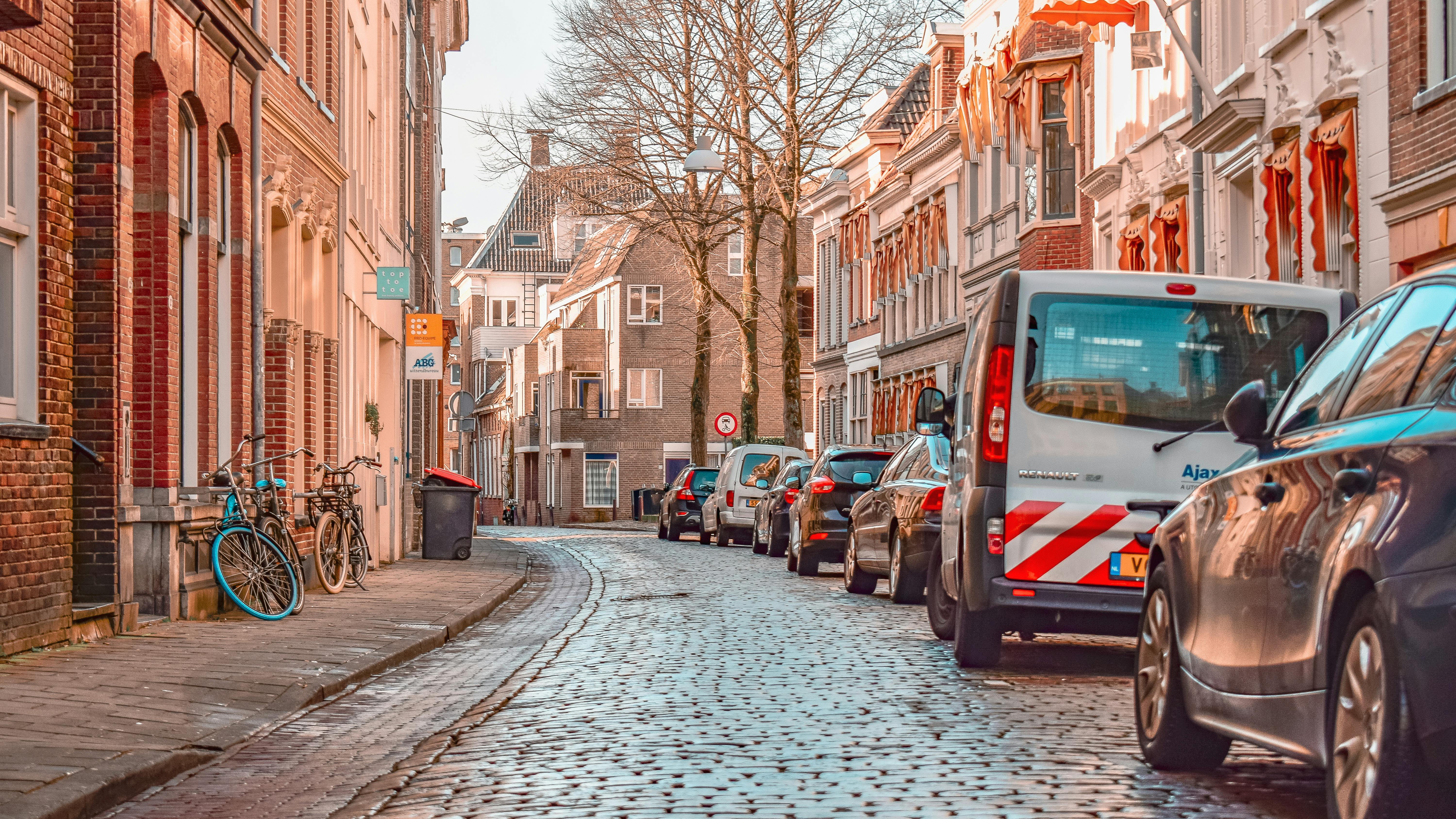 Vehicles and bikes parked up on a residential street in Groningen. Houses line either side, with more in the distance.